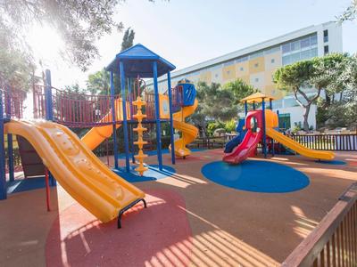 Kleurrijke speeltuin met glijbanen naast een hotelgebouw op een zonnige dag.