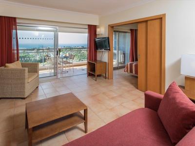 Lichte hotelkamer met zithoek, balkon en zeezicht.