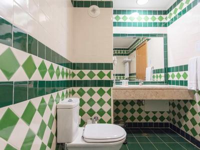 Badkamer met witte en groene tegels, toilet en wastafel met spiegel.