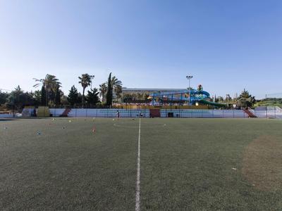 Freundliches Fußballfeld mit Toren und Tribünen bei klarem Himmel.