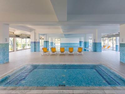 Leeg binnenzwembad in een lichte, open ruimte met gele stoelen en grote ramen.