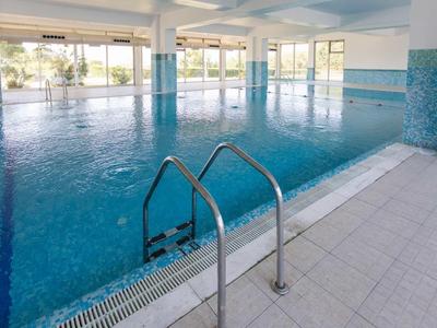 Overdekt zwembad met trap, grote ramen en blauw-witte tegels in een modern gebouw.