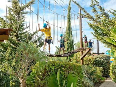 Mensen steken een touwenparcours over met veiligheidsbanden in een groene hotelomgeving bij heldere lucht.