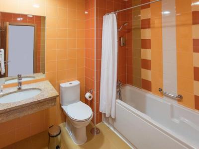 Hotelbadkamer met oranje tegels, wit bad, toilet en wastafel.