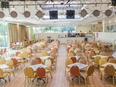 Grote evenementenhal met rijen tafels en stoelen, podium aan de voorkant met verlichting.