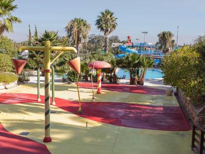 Waterspeeltuin voor kinderen met fonteinen en palmbomen bij het zwembad in zonnige omgeving