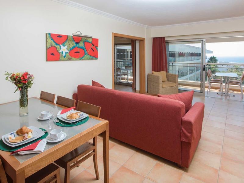 Woonkamer met rode bank, eetgedeelte en balkon met zeezicht.