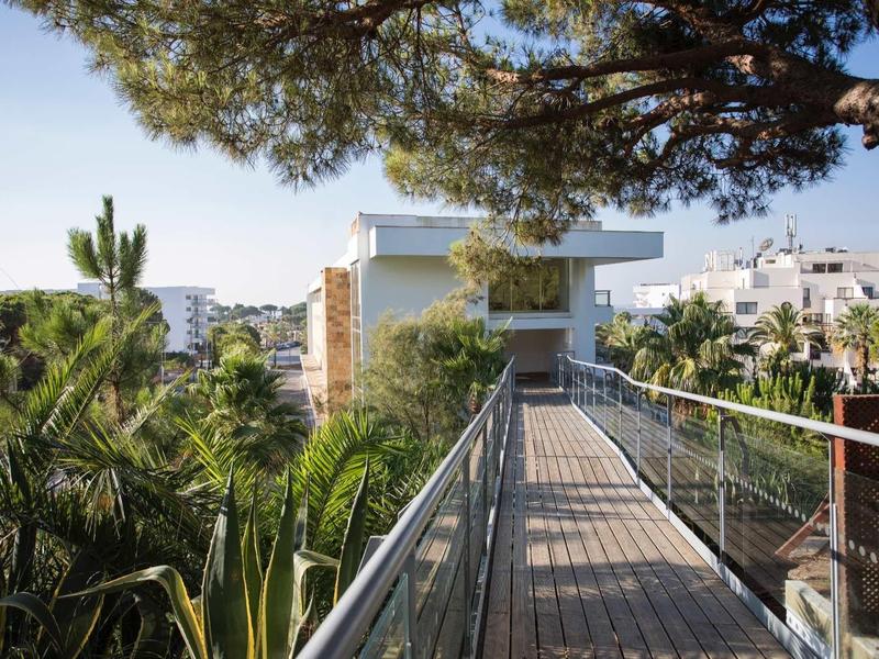 Moderne hotelgang met glazen balustrade omgeven door weelderig groen en palmbomen.