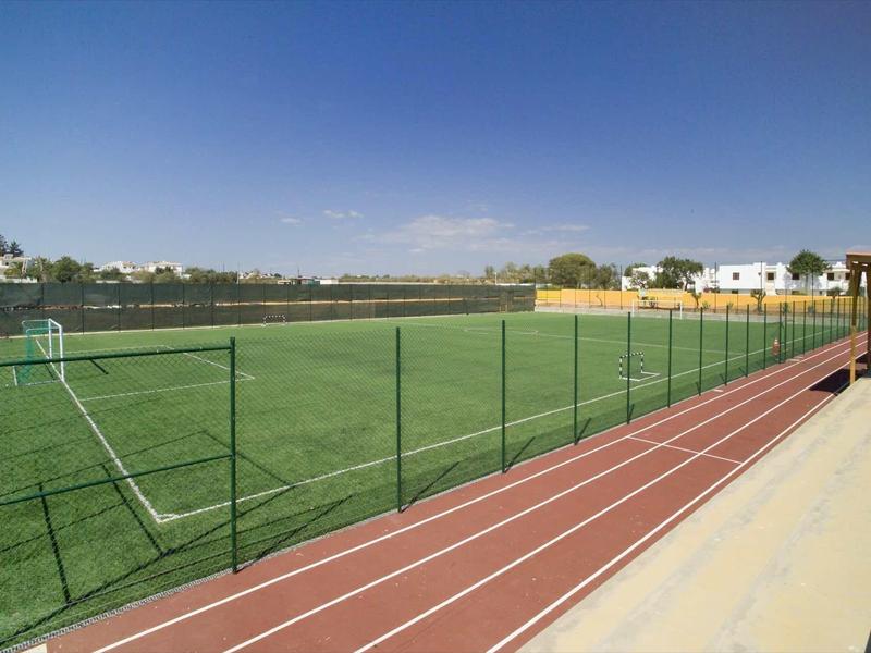 Een sportveld met groen kunstgras naast een rode hardloopbaan onder een heldere blauwe lucht.
