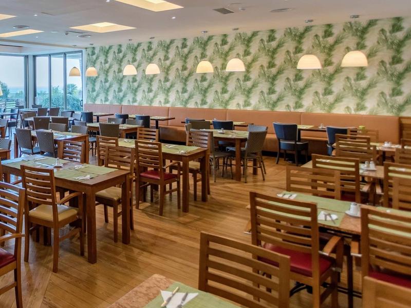 Licht restaurant met houten tafels, stoelen en botanische wanddecoratie.