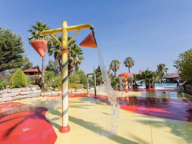 Kinderen water speelplaats met kleurrijke watersproeiers en palmbomen onder een blauwe lucht