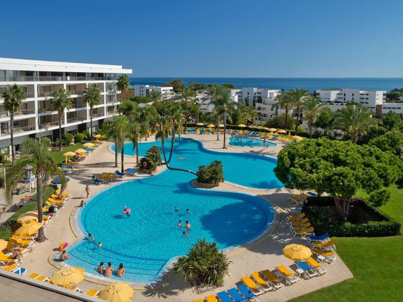 Hotelzwembad met parasols, ligstoelen en uitzicht op zee onder een heldere hemel
