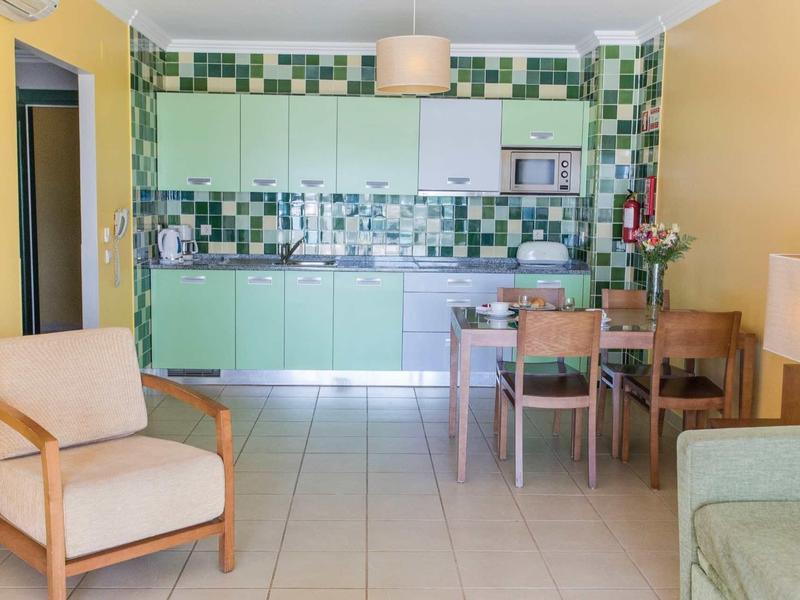 Lichte hotelkeuken met groene geruite tegels, eettafel en comfortabele zitplaatsen.