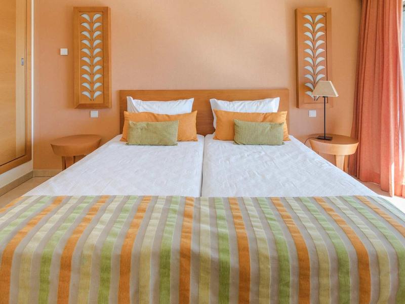 Modern tweepersoonsbed met oranje-groene bedsprei in een lichte, gezellige kamer.