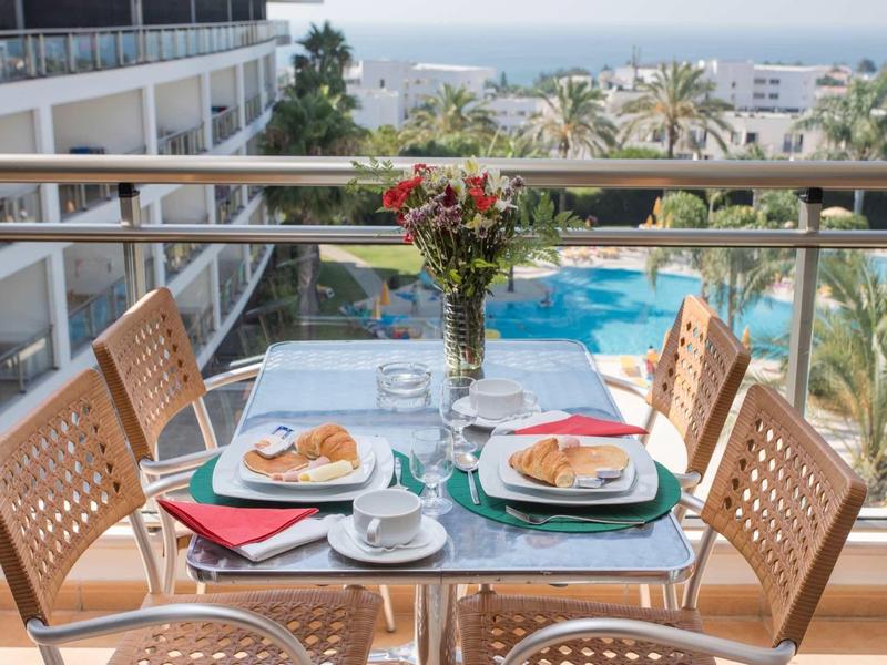 Balkontafel met ontbijt met uitzicht op een zwembad en palmbomen bij de zee.