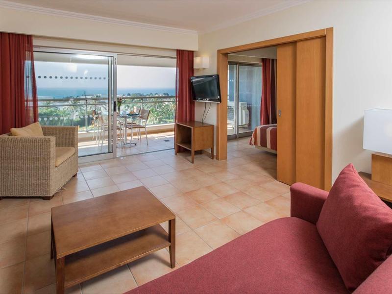 Lichte hotelkamer met zithoek, balkon en zeezicht.