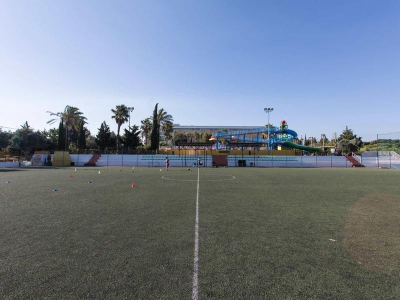 Een groot leeg voetbalveld met een heldere lucht en gebouwen op de achtergrond.