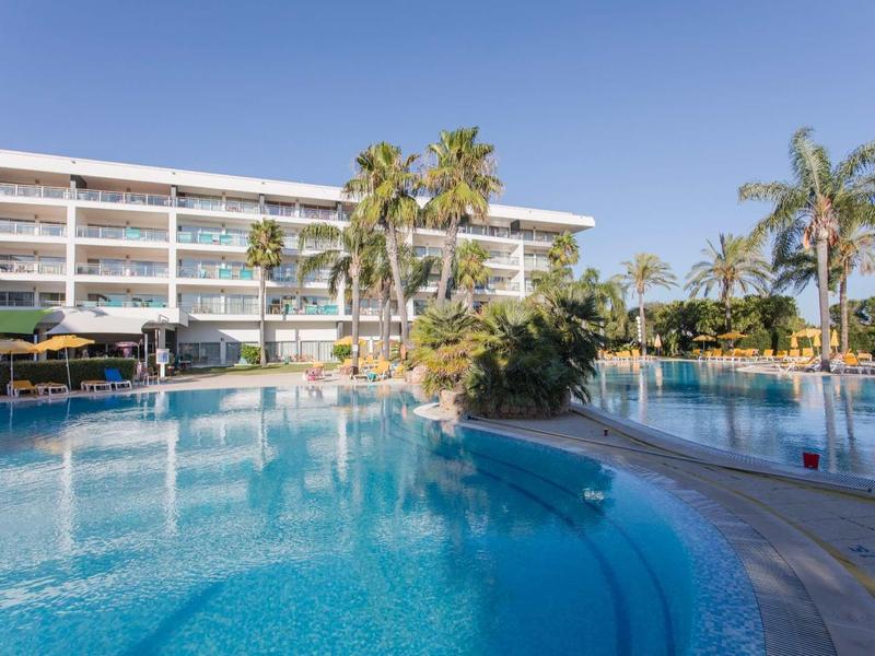 Groot buitenzwembad voor een meerlaagshotel met palmbomen en parasols onder een heldere hemel.