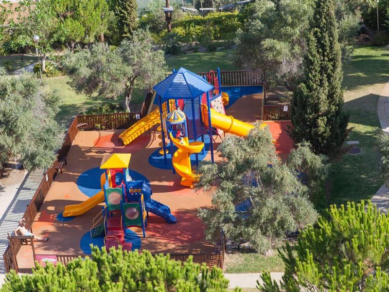 Kleurrijke kinderspeelplaats met glijbanen en klimrekken in een park met bomen.