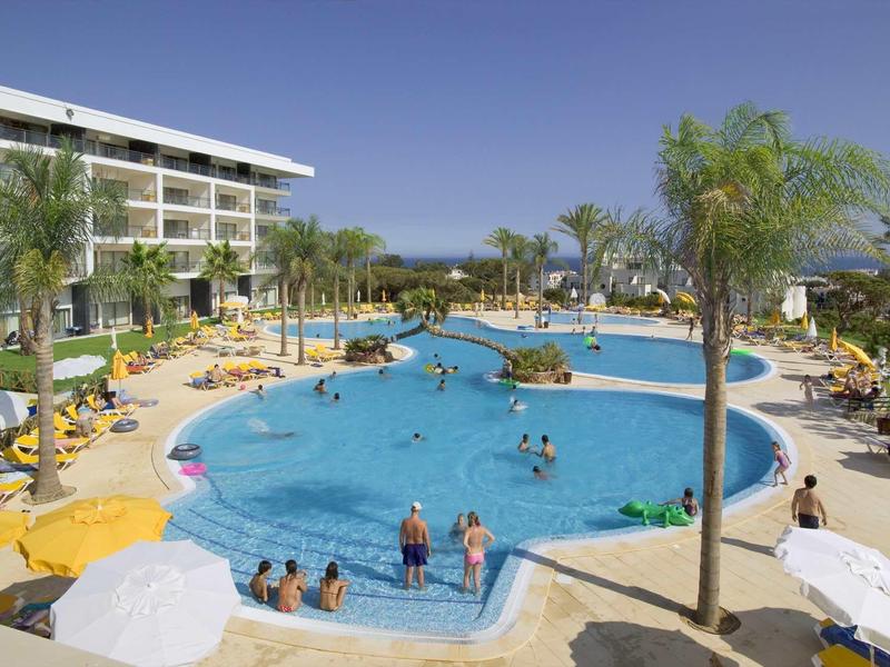 Groot hotelzwembad met parasols, ligstoelen en een met palmen omzoomd zwembadgebied.