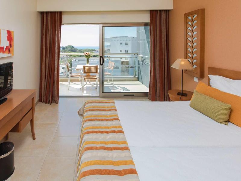 Hotelkamer met tweepersoonsbed, tv, bureau en balkon met zeezicht.