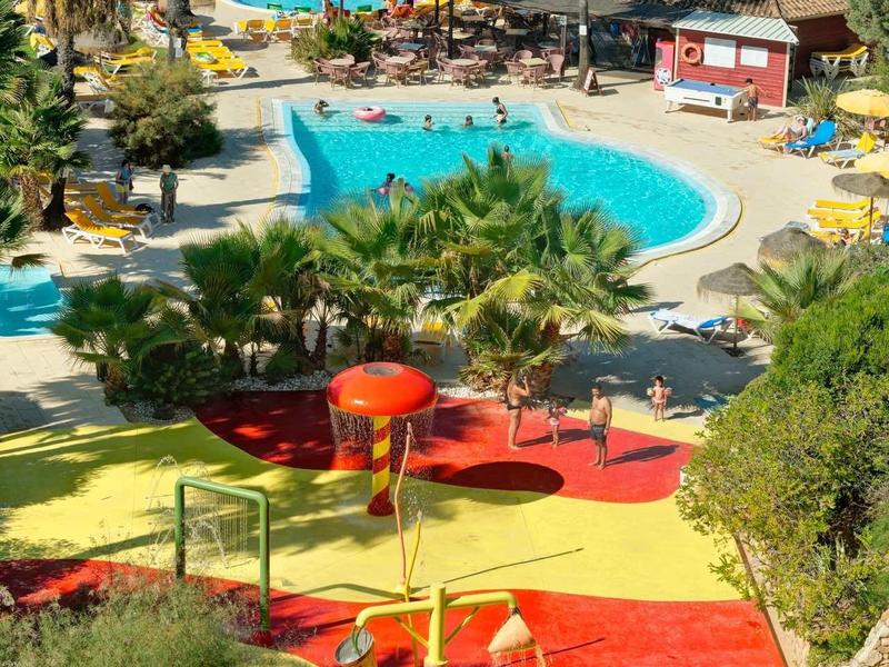 Uitzicht op een kleurrijk waterspeelpark met meerdere zwembaden en parasols in een tropisch resort.