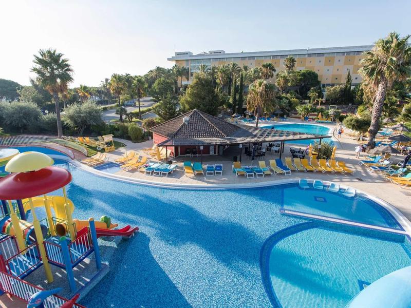 Groot buitenzwembad met glijbanen en parasols omringd door palmbomen en hotelgebouwen.