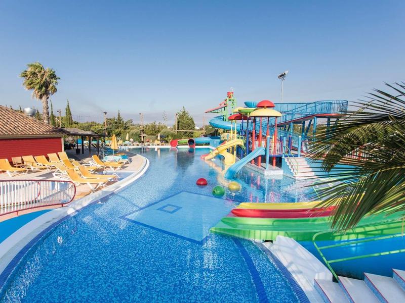 Waterpark met zwembad, kleurrijke glijbanen en ligstoelen onder een heldere lucht.