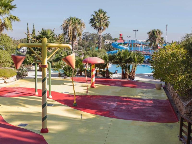 Waterspeeltuin voor kinderen met fonteinen en palmbomen bij het zwembad in zonnige omgeving