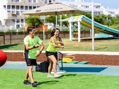 Zwei Personen gehen auf einem Spielplatz mit Rutsche und Sonnenschirm bei Tageslicht.