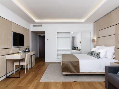 Groot rond zwembad omgeven door parasols en ligstoelen in een tuin met uitzicht op de stad.