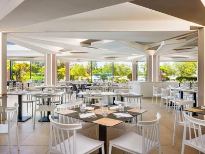 Salle à manger moderne et lumineuse avec chaises blanches et grandes fenêtres donnant sur la verdure.