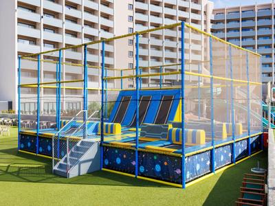 Trampolín colorido al aire libre frente a un edificio de hotel sobre césped artificial.
