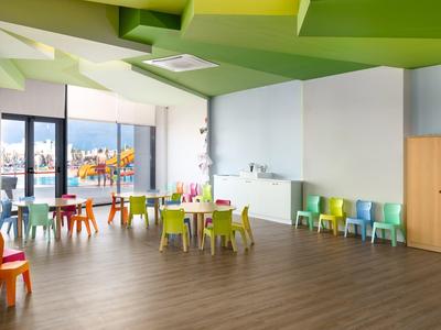 Lichte groene recreatieruimte met kleurrijk kindermeubilair en groot raam met uitzicht.