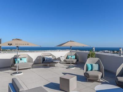 Terraza moderna en la azotea con asientos, sombrillas y vista al mar bajo un cielo azul claro.