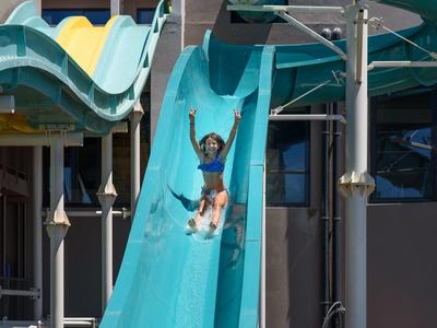 Kind glijdt met één arm in de lucht van een blauwe glijbaan af.