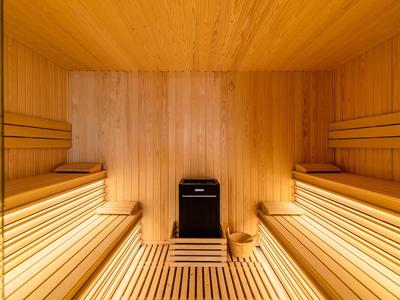 Lichte houten sauna met twee bankrijen en een houtkachel in het midden.