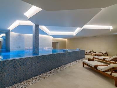 Moderne binnenzwembad met een blauw bad en comfortabele ligstoelen.