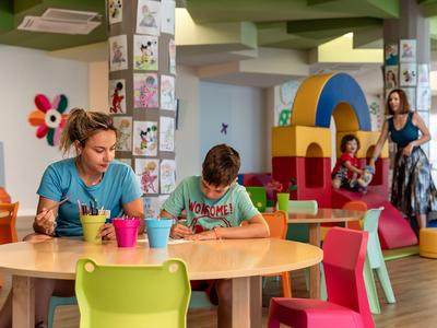 Kinderen spelen en tekenen in een kleurrijke binnenruimte met speeltoestel en zitplaatsen.