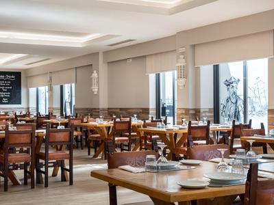 Licht, modern restaurant met houten tafels en stoelen, gedekt met borden en glazen.