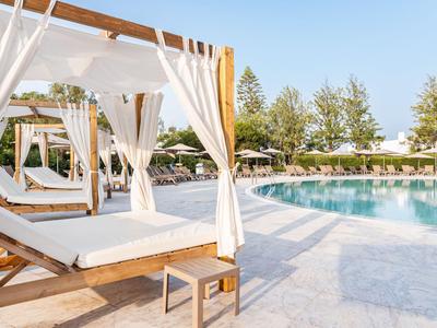 Luxuriöse hölzerne Tagesbetten mit weißen Vorhängen neben einem klaren Pool unter blauem Himmel.