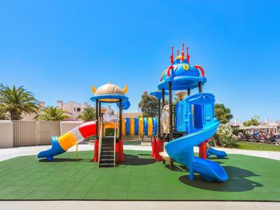 Kleurrijke speeltuin met glijbanen en klimnetten op groen gras onder een heldere hemel.