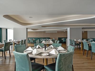 Moderne eetzaal met ronde tafels, groene stoelen en elegant gedekte plaatsen.