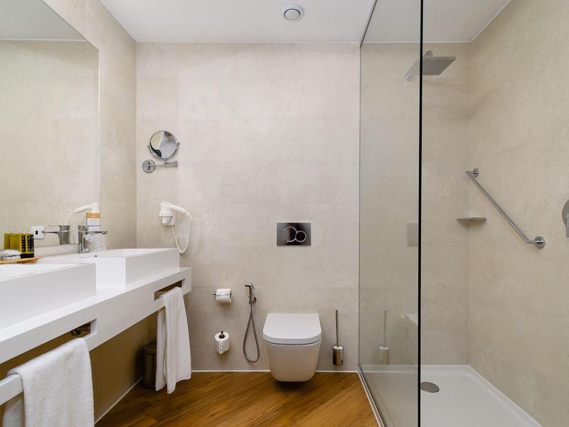 Moderne badkamer met inloopdouche, toilet en dubbele wastafel in neutrale tinten.