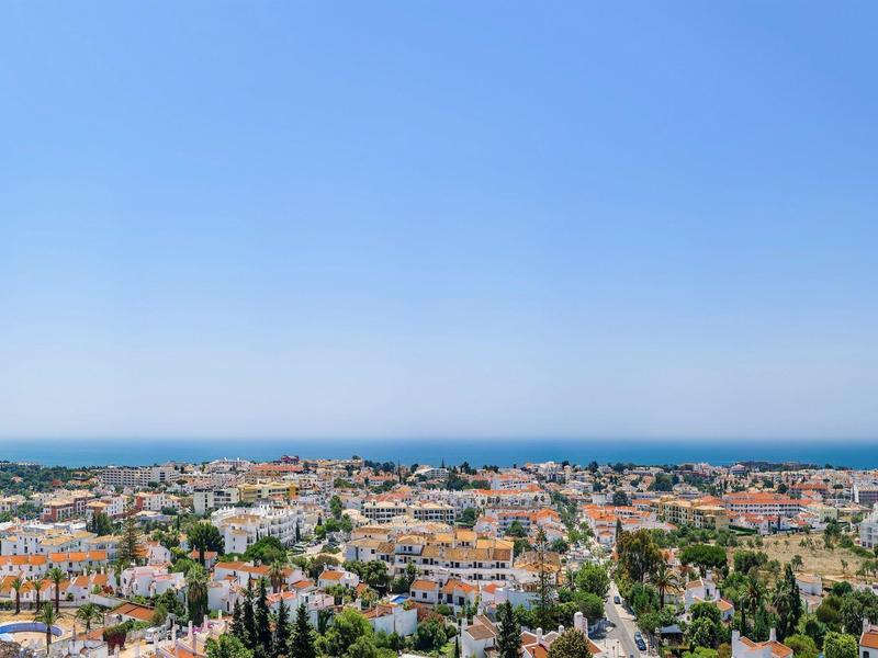 Uitzicht op een stad met rode daken aan zee onder een heldere blauwe lucht.