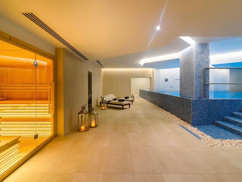 Moderne wellnessruimte met sauna, ligstoelen en binnenzwembad in warm licht.