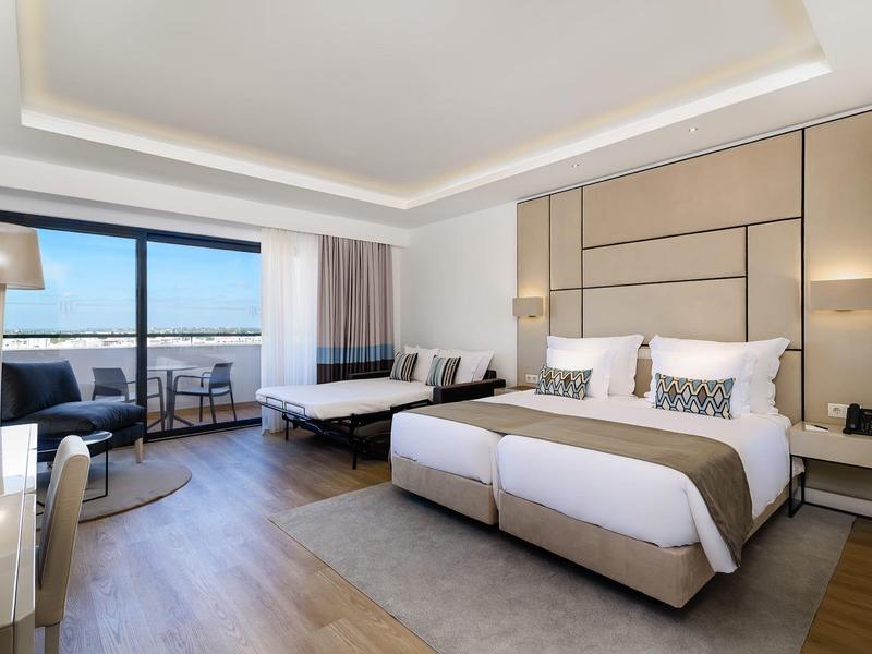 Licht, modern restaurant met grote ramen en witte stoelen, omgeven door groen.