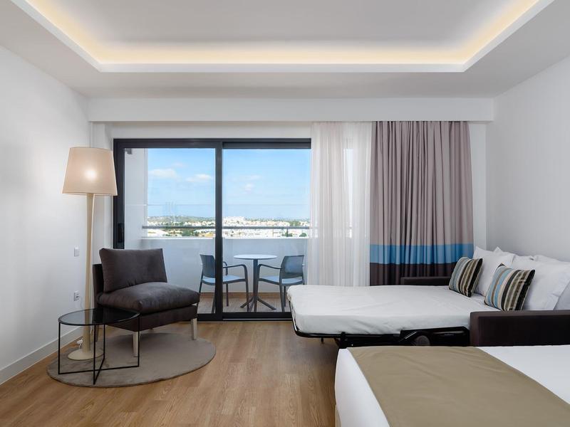 Modern hotelkamer met twee bedden, fauteuils en een balkon met uitzicht op zee.