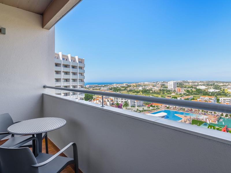 Balkon met stoelen en tafel, uitzicht op stad en zee in de verte.