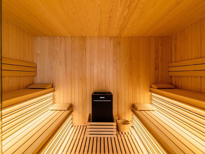 Lichte houten sauna met twee bankrijen en een houtkachel in het midden.